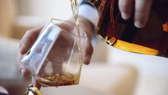 person pouring whiskey into a tumbler glass; can you drink while on accutane?