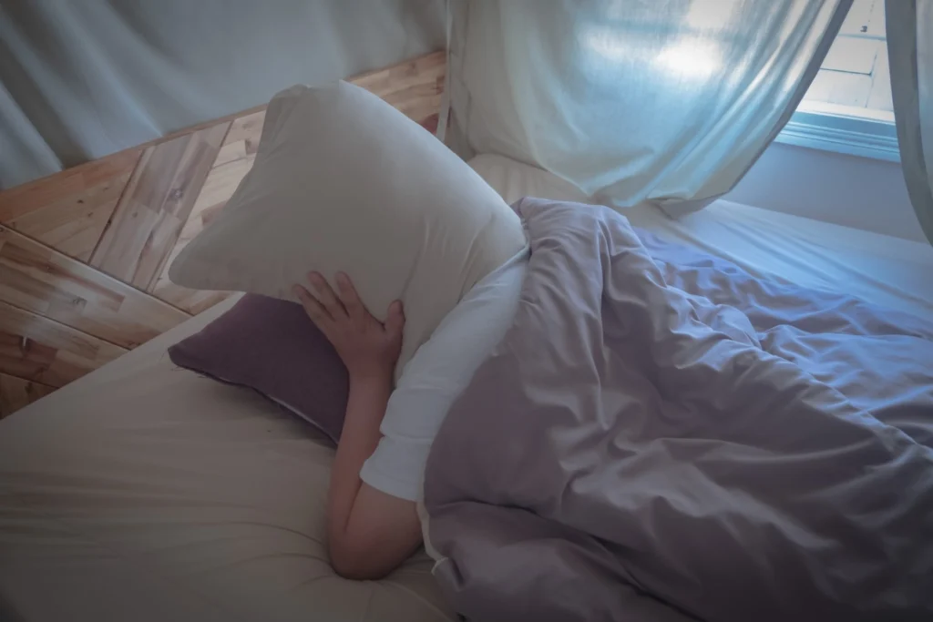 person with insomnia covers their head with pillows while trying to sleep
