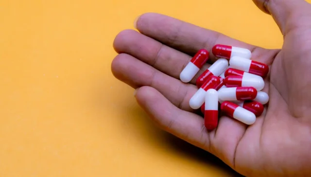 Is Lyrica a Narcotic? A hand holding red and white pill capsules in front of a yellow background.