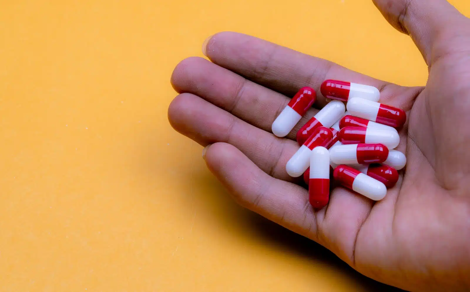 Is Lyrica a Narcotic? A hand holding red and white pill capsules in front of a yellow background.