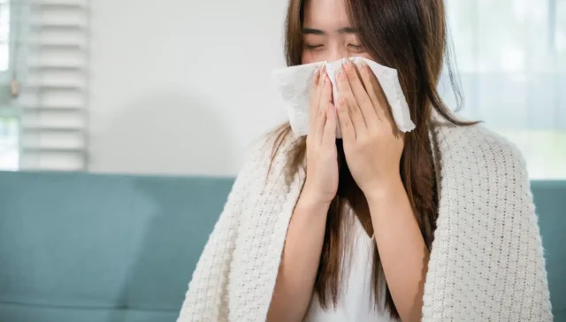 Is NyQuil Bad For You? A woman blowing her nose wrapped in a blanket.