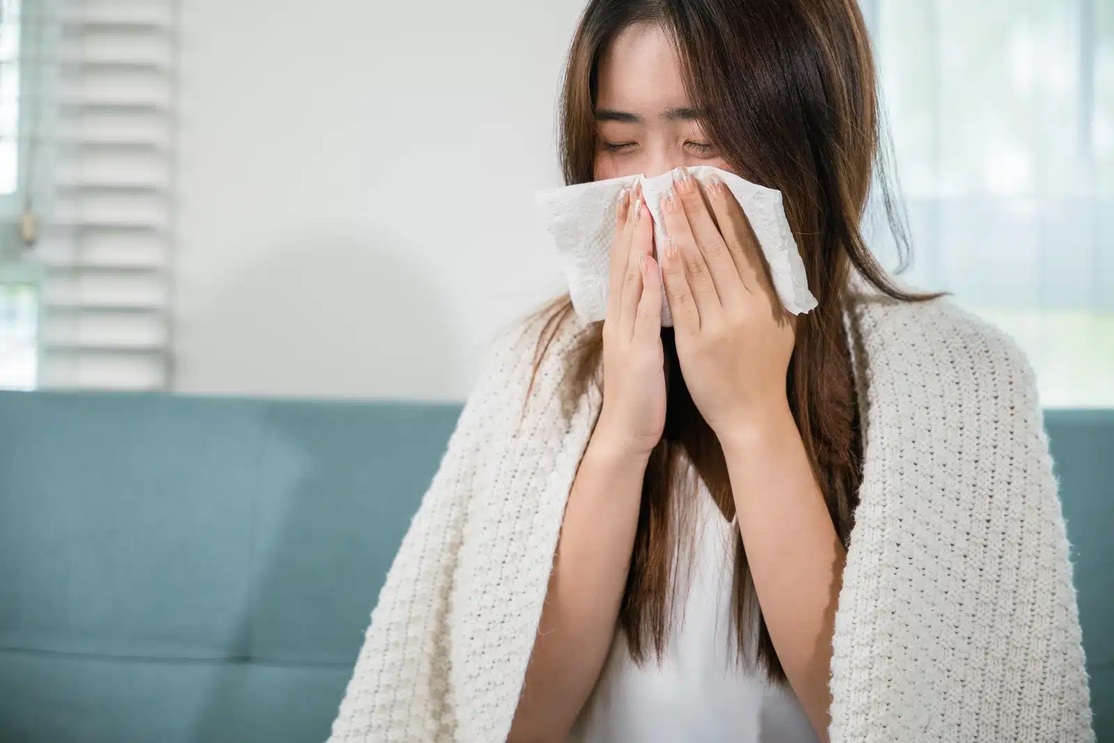 Is NyQuil Bad For You? A woman blowing her nose wrapped in a blanket.