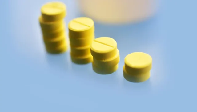 Can You Get a Meloxicam High? Yellow pills stacked in a row on a blue surface.