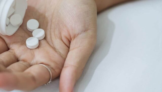 How Long Does Meloxicam Stay In Your System? A hand extended palm up with white pills being poured into it
