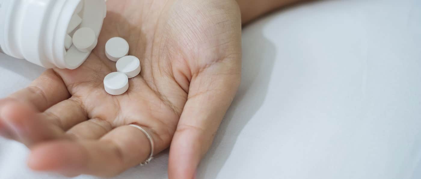 How Long Does Meloxicam Stay In Your System? A hand extended palm up with white pills being poured into it