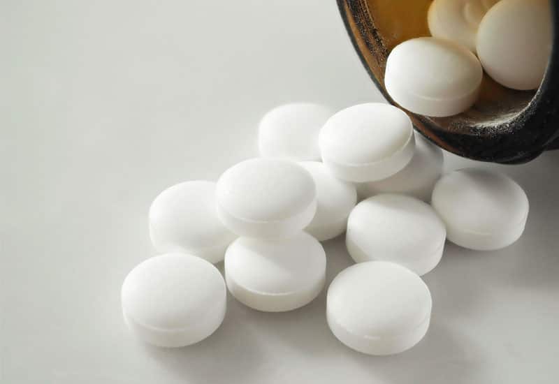 White pills spilling out of a brown pill bottle onto a white surface