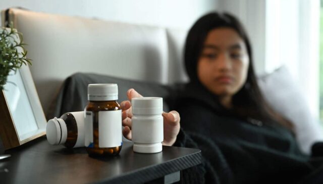 Is Concerta the Same as Ritalin? A woman in bed reaching for a pill bottle on her nightstand