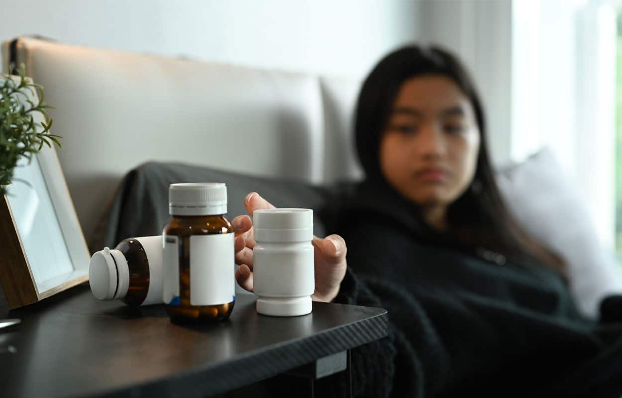  Is Concerta the Same as Ritalin? A woman in bed reaching for a pill bottle on her nightstand
