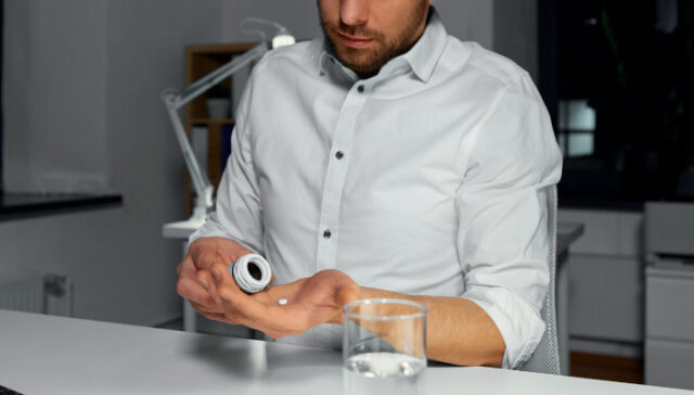 Exhausted office worker at a desk with Adderall pills, symbolizing stimulant dependence from performance pressure
